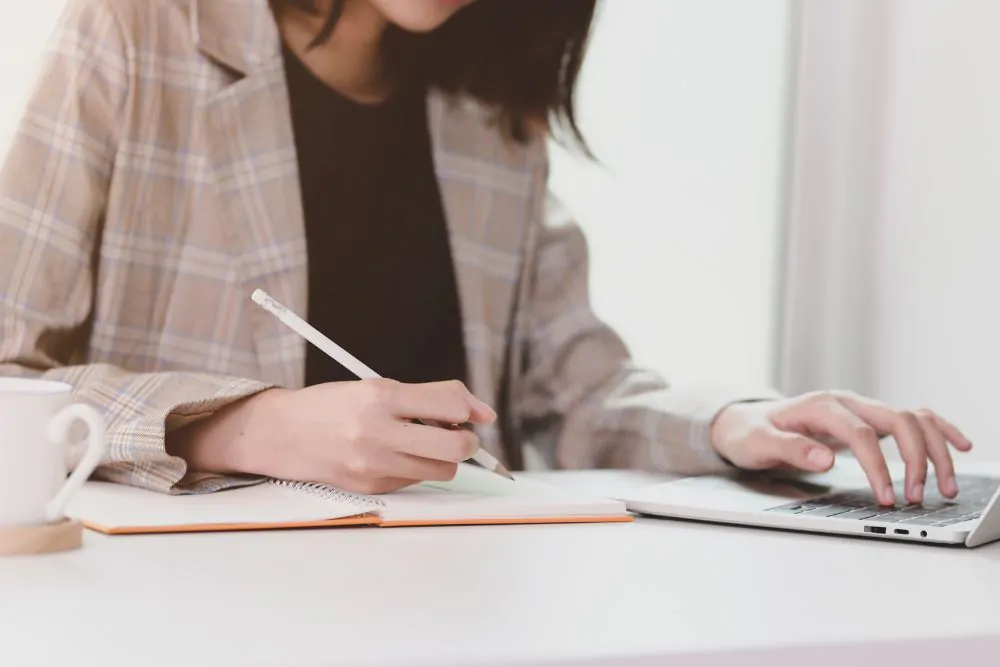 Giovane imprenditrice motivata che pianifica la sua strategia mentre digita su un computer portatile e scrive su un taccuino