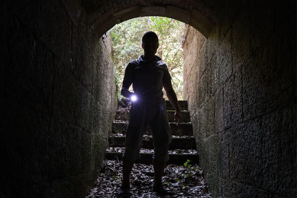 Il giovane con una torcia elettrica entra nel tunnel di pietra e guarda nella foto scura e monocromatica